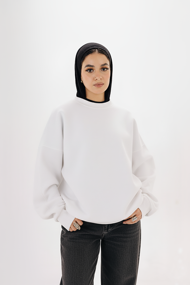 Female model wearing white oversized boxy crewneck sweatshirt with hijab — studio background


