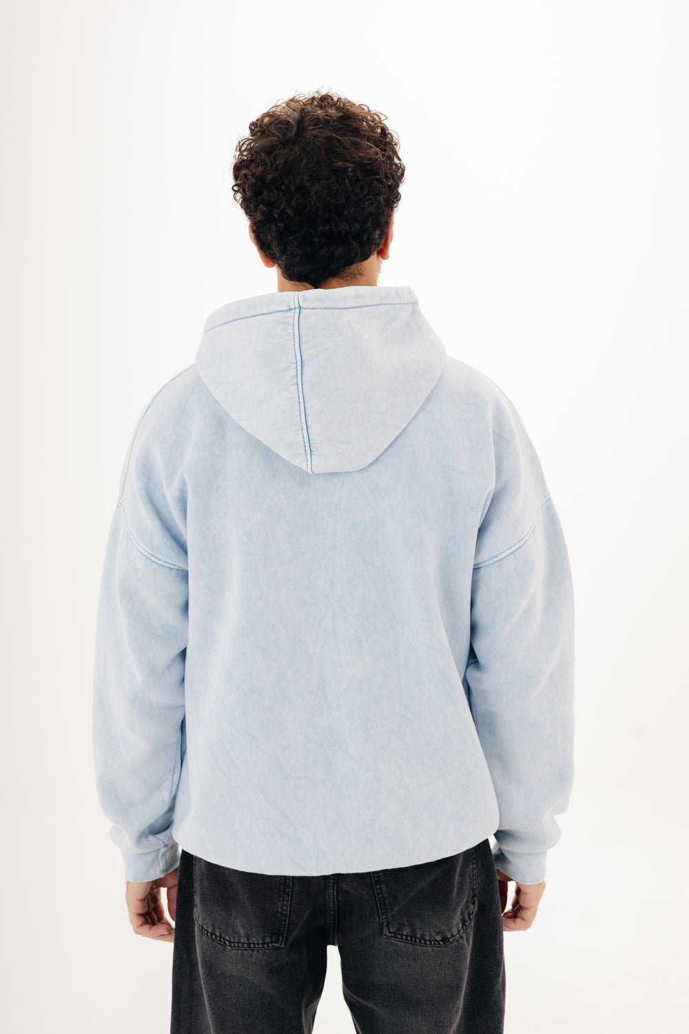 Back view of baby blue washed oversized hoodie on male model — plain white studio background
