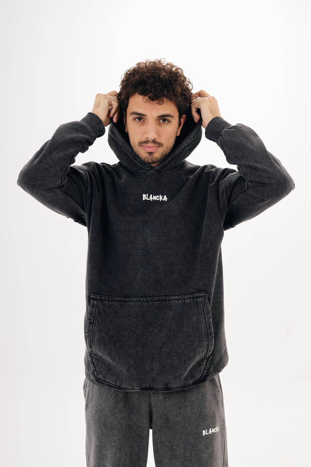 Close-up of male model wearing charcoal acid wash hoodie with hood up — studio background
