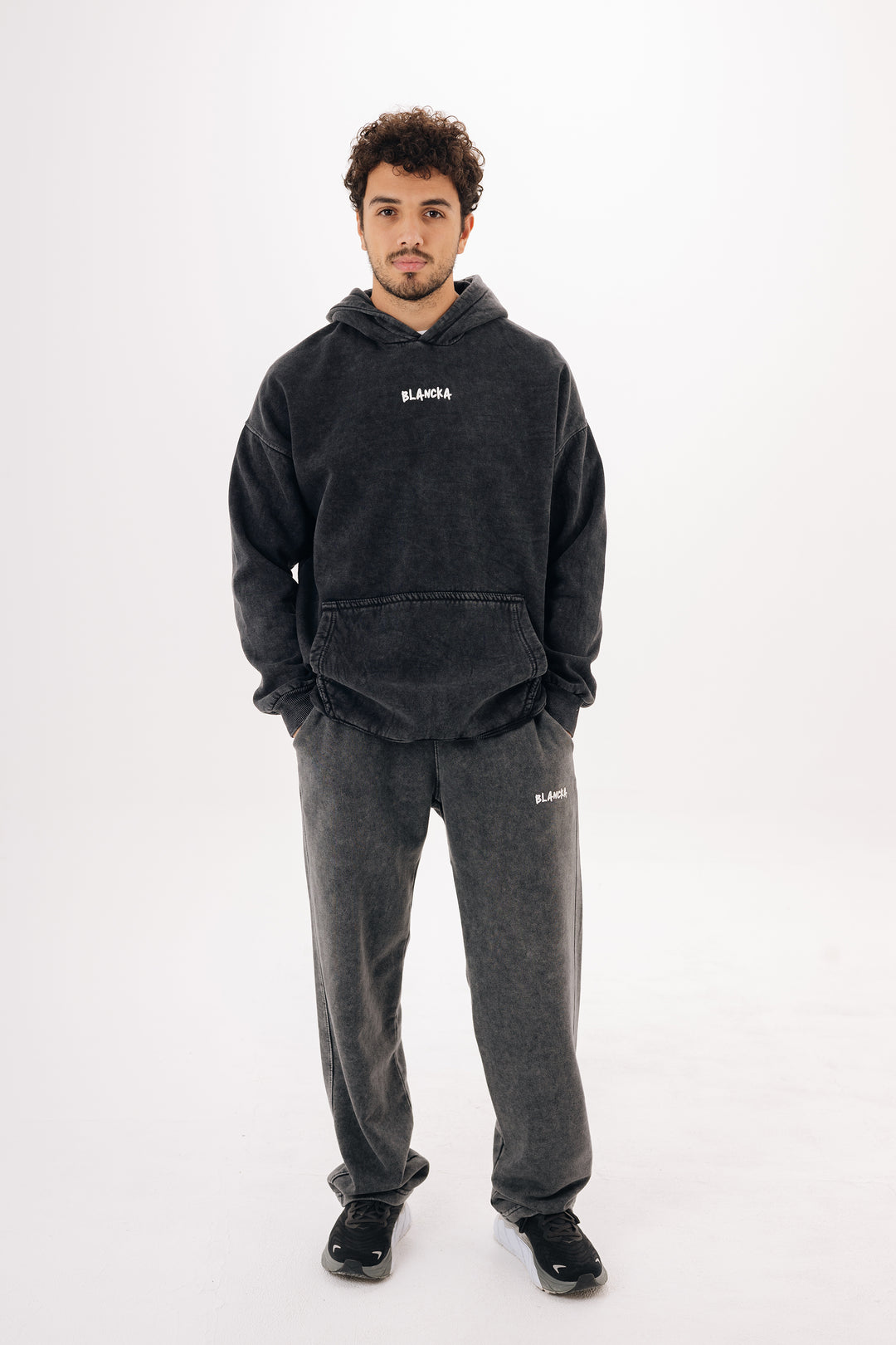Male model wearing charcoal washed oversized hoodie with BLANCKA print — full body studio shot
