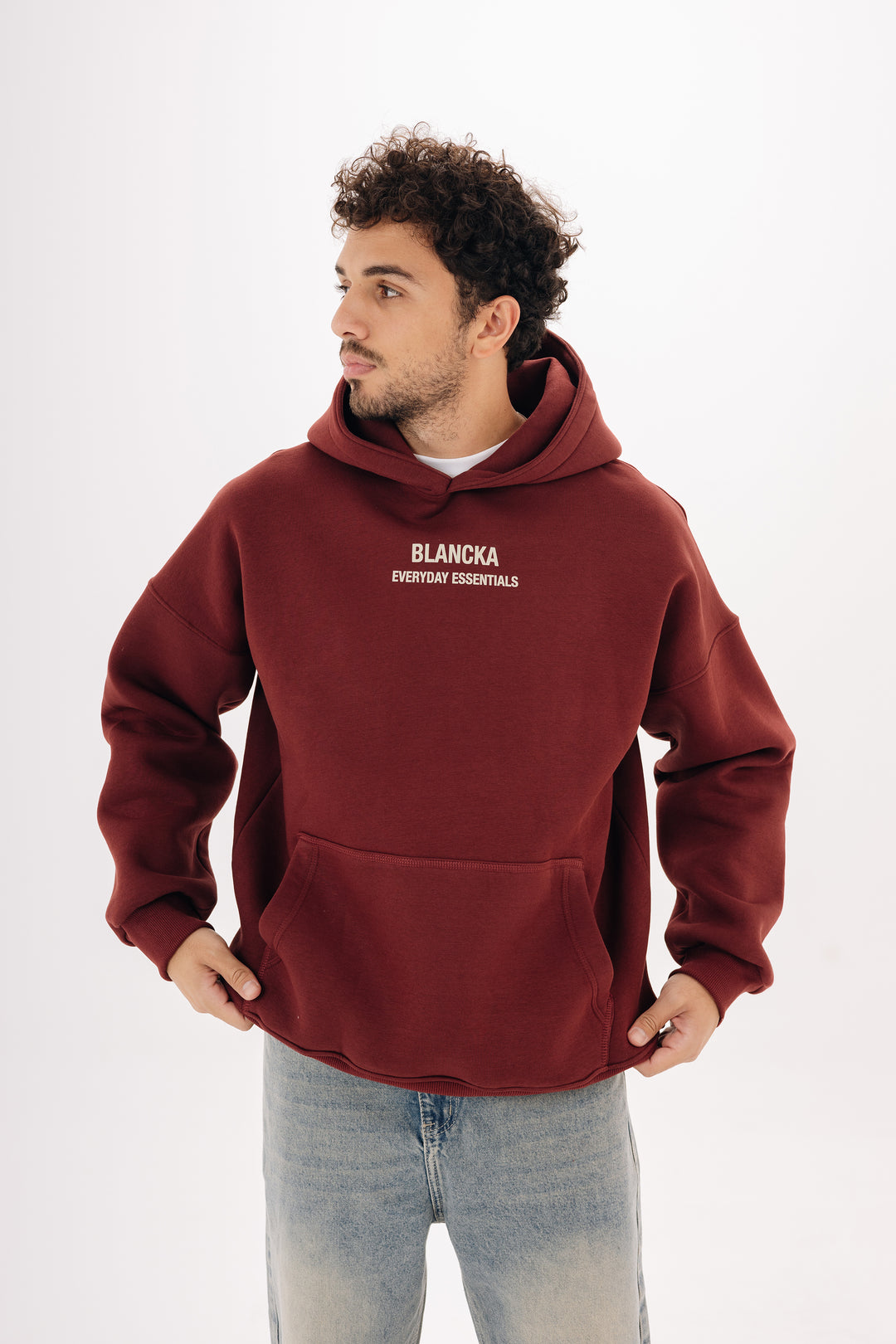Male model wearing burgundy boxy hoodie with front chest print — studio background
