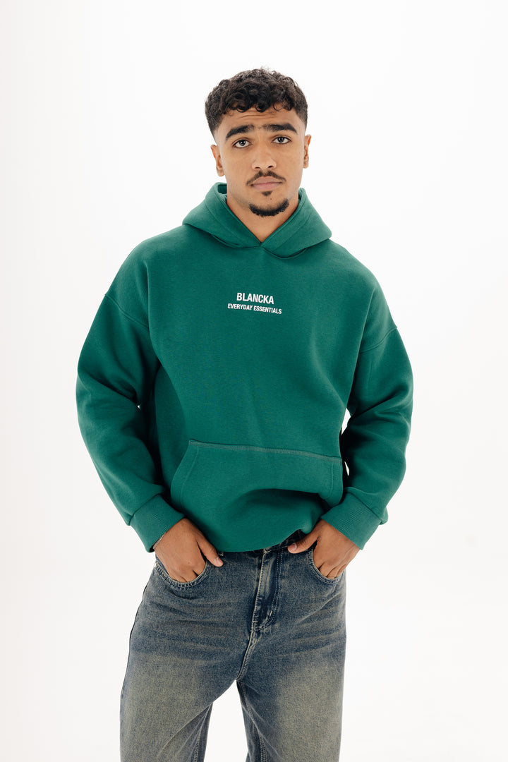 Male model wearing green boxy Blancka hoodie with front print — studio white background
