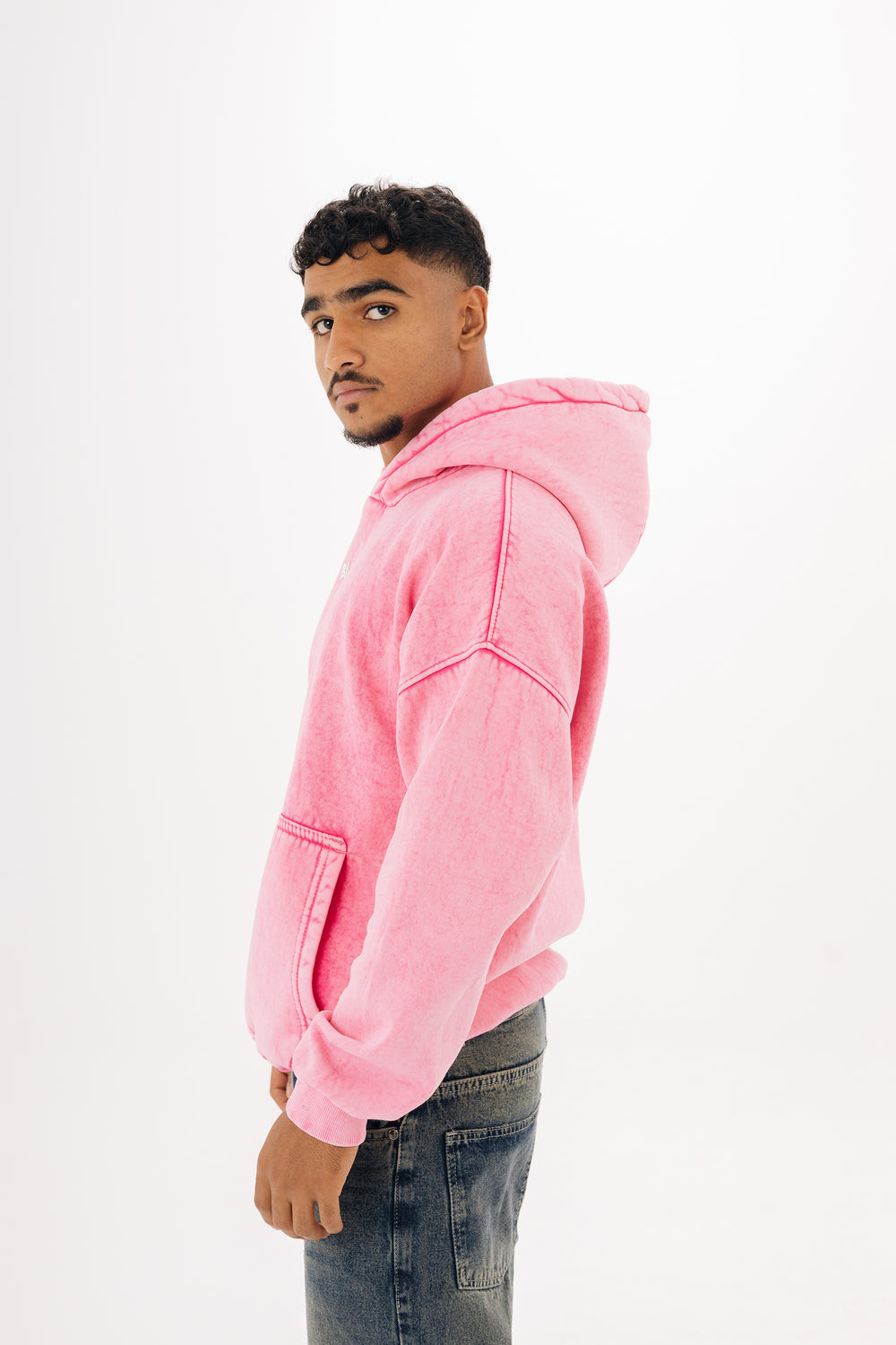 Side view of male model in pink acid wash hoodie with front pocket — studio background

