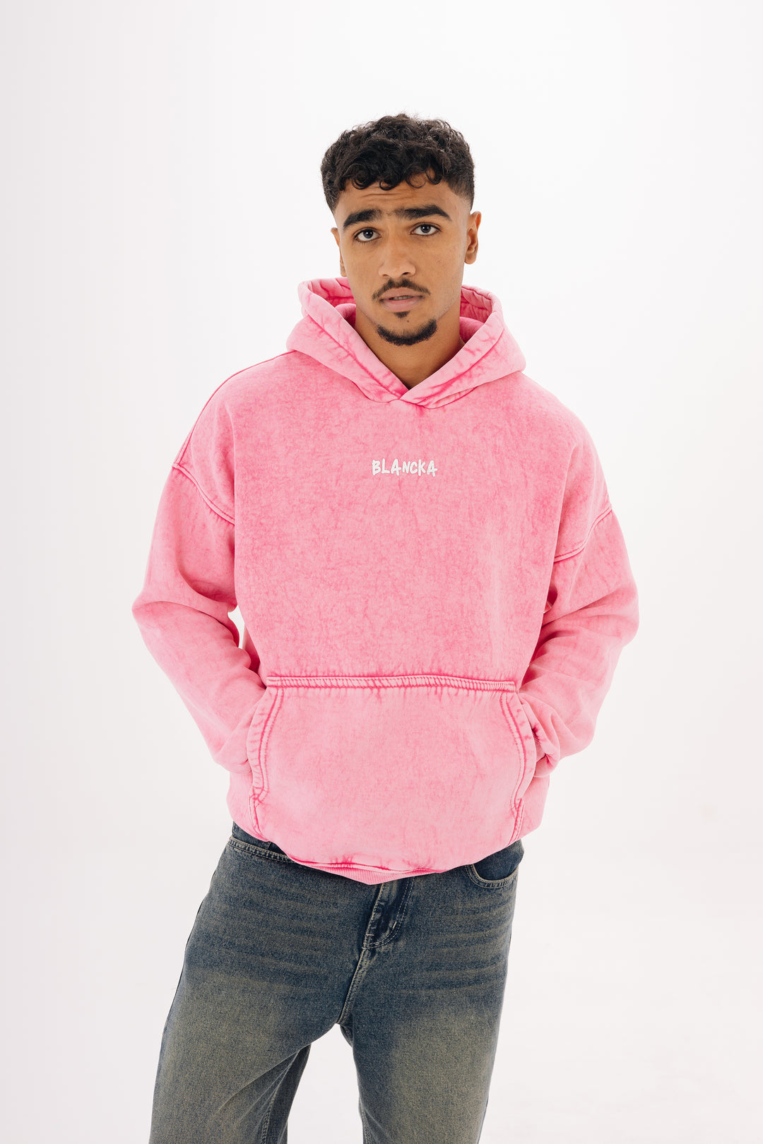 Male model wearing pink washed oversized hoodie with BLANCKA print — studio white background
