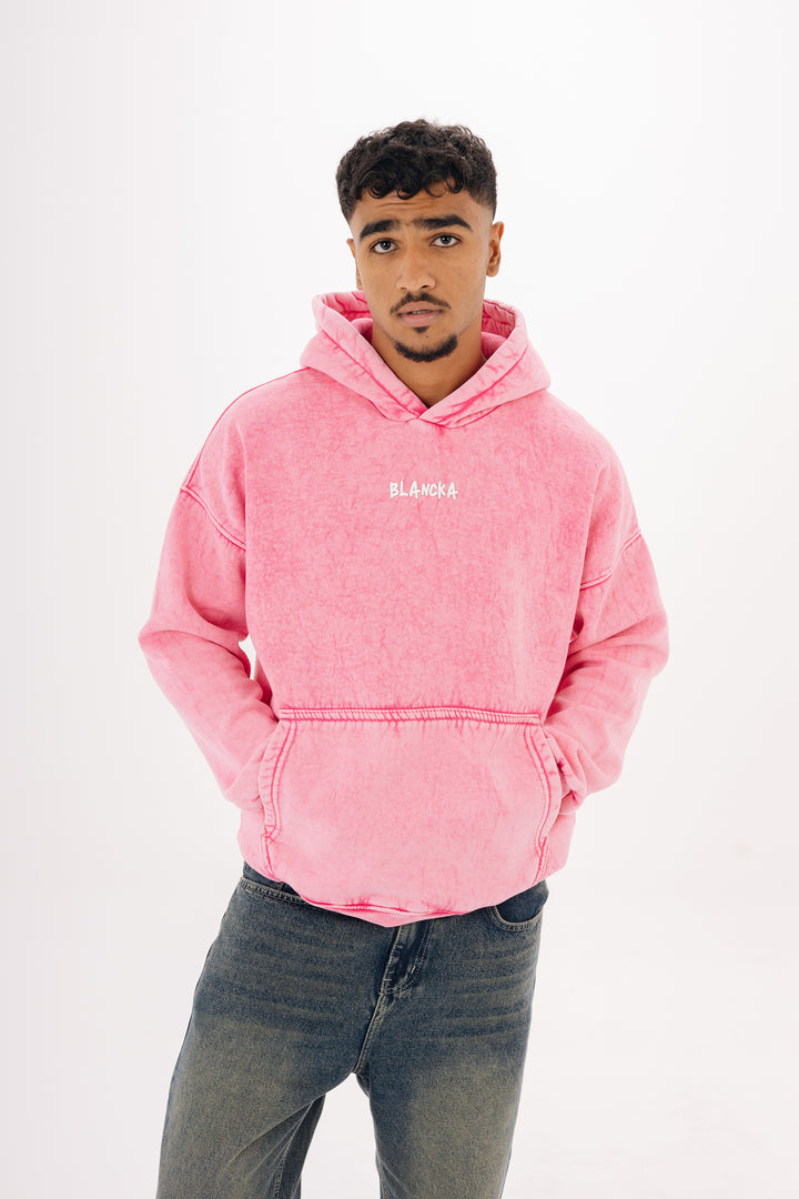 Male model wearing pink washed oversized hoodie with BLANCKA print — studio white background
